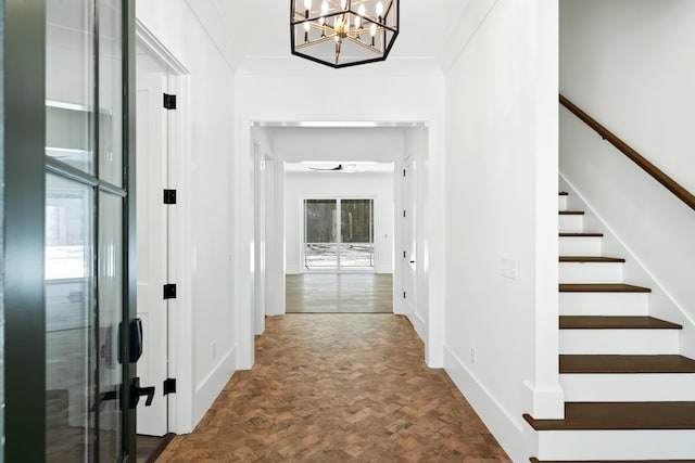 hallway with ornamental molding, a chandelier, baseboards, and stairs