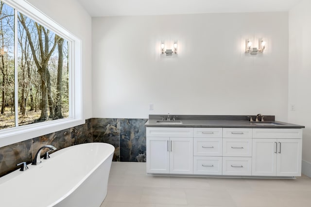 bathroom with double vanity, a freestanding tub, a sink, and tile walls