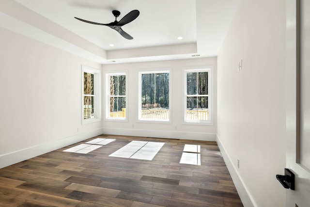 unfurnished room with a tray ceiling, recessed lighting, baseboards, and wood finished floors