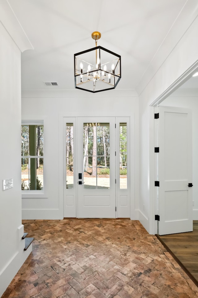 doorway featuring baseboards, visible vents, brick floor, crown molding, and a chandelier