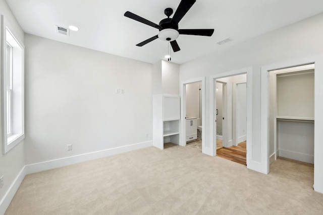 unfurnished bedroom with light colored carpet, a walk in closet, visible vents, and baseboards