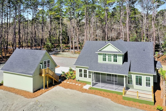 view of front of property featuring a sunroom, stairs, driveway, roof with shingles, and a view of trees