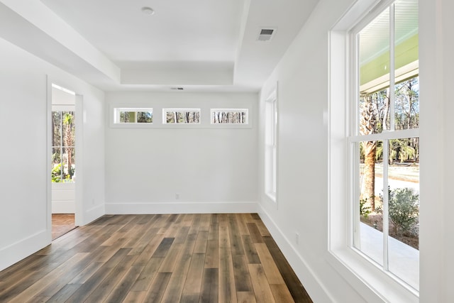 unfurnished room featuring dark wood-style floors, a raised ceiling, visible vents, and baseboards