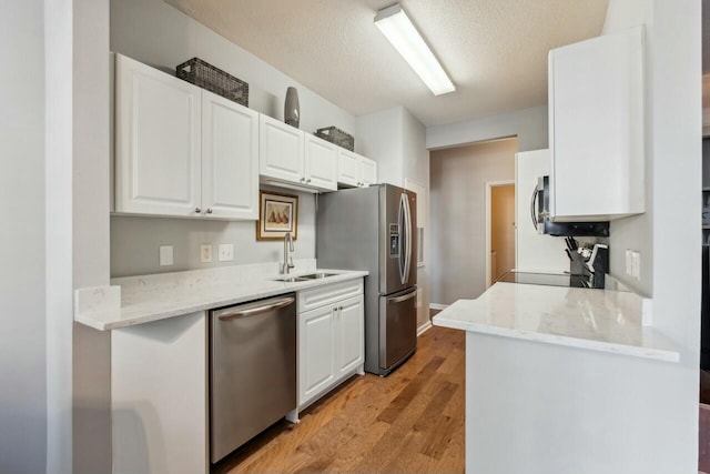 kitchen featuring light wood-type flooring, appliances with stainless steel finishes, white cabinets, and a sink