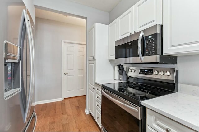 kitchen with stainless steel appliances, white cabinets, light wood-style floors, and light stone countertops