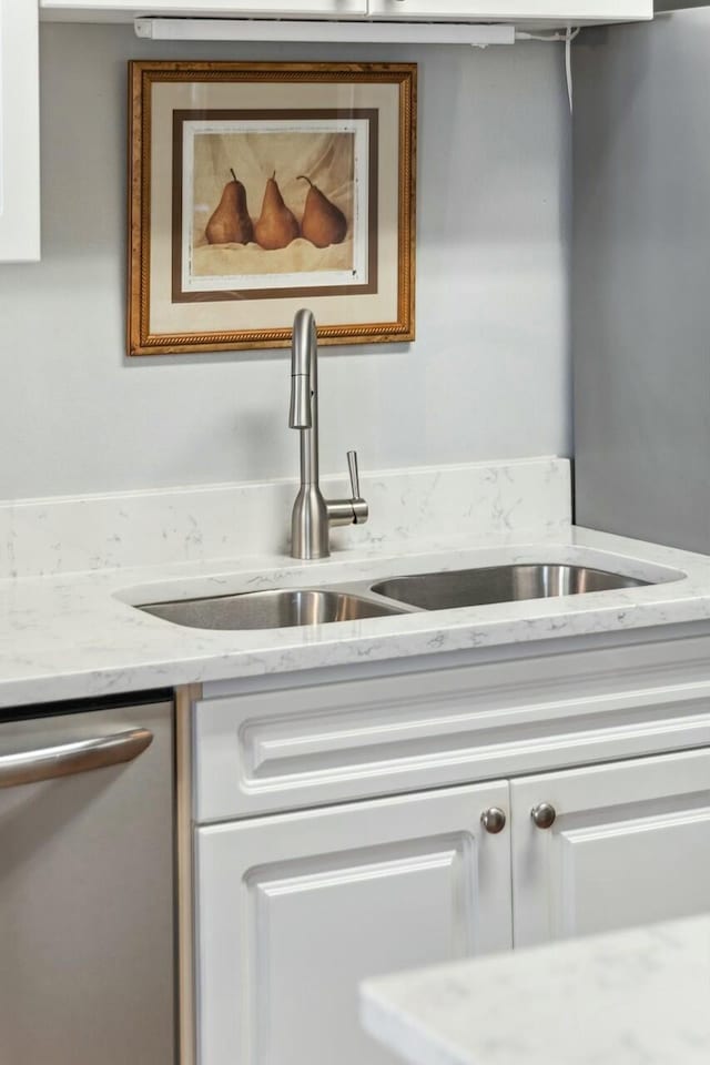 kitchen with stainless steel dishwasher, white cabinetry, light stone counters, and a sink