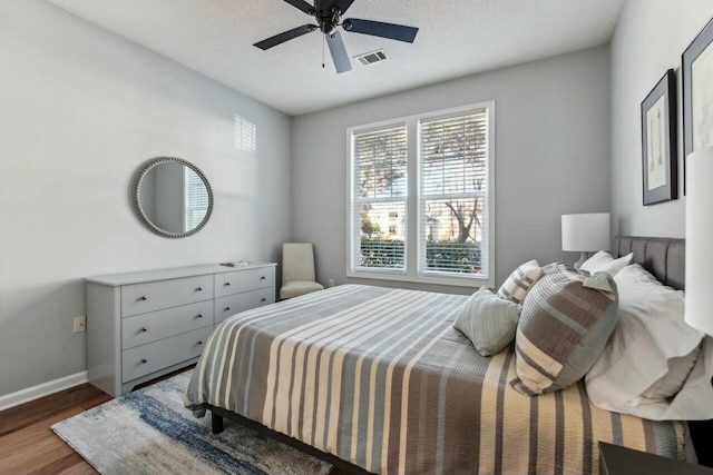 bedroom with a ceiling fan, wood finished floors, visible vents, and baseboards