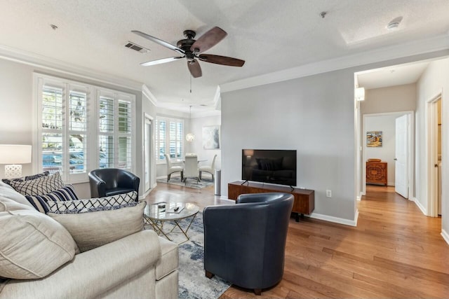 living area featuring light wood-type flooring, baseboards, visible vents, and ornamental molding