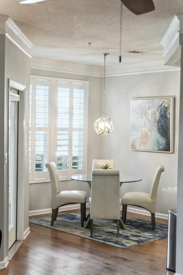 dining space featuring a textured ceiling, ornamental molding, and wood finished floors