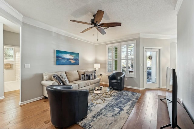 living room with a textured ceiling, a ceiling fan, baseboards, ornamental molding, and hardwood / wood-style floors