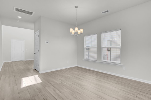 spare room with light wood finished floors, visible vents, and a notable chandelier