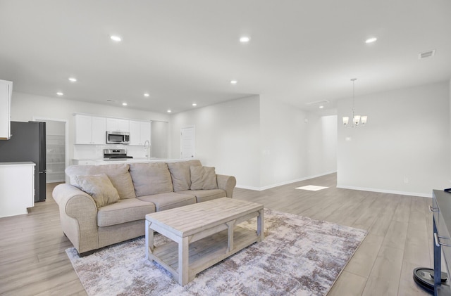 living room with recessed lighting, baseboards, light wood finished floors, and an inviting chandelier