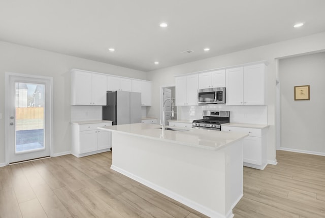 kitchen featuring an island with sink, appliances with stainless steel finishes, light countertops, light wood-style floors, and white cabinetry