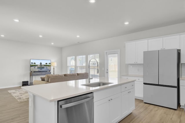 kitchen featuring a kitchen island with sink, a sink, white cabinets, stainless steel dishwasher, and freestanding refrigerator