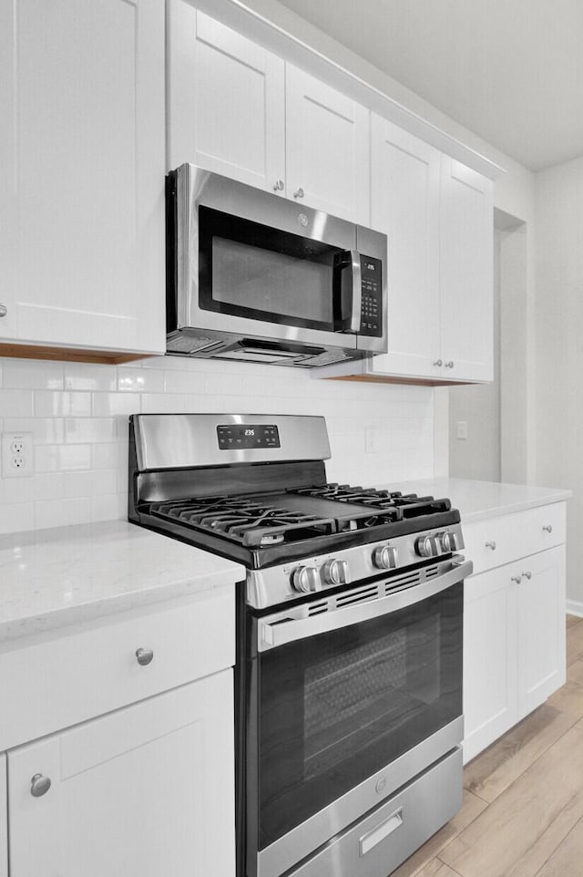 kitchen featuring light stone countertops, white cabinetry, stainless steel appliances, and backsplash