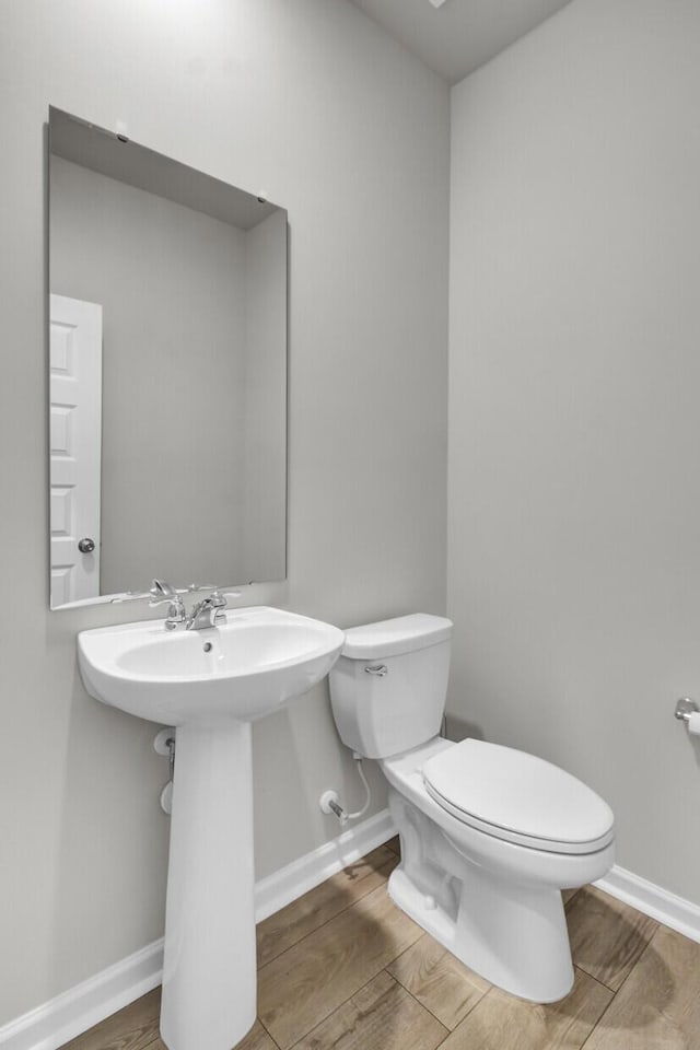 half bathroom with wood finished floors, toilet, and baseboards