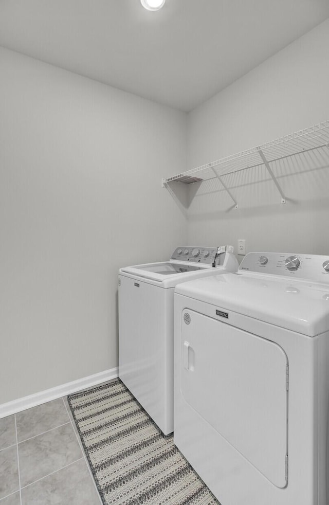 clothes washing area with laundry area, washer and clothes dryer, baseboards, and light tile patterned floors