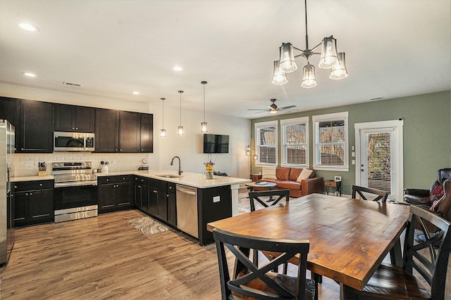 kitchen with sink, light wood-type flooring, pendant lighting, stainless steel appliances, and decorative backsplash