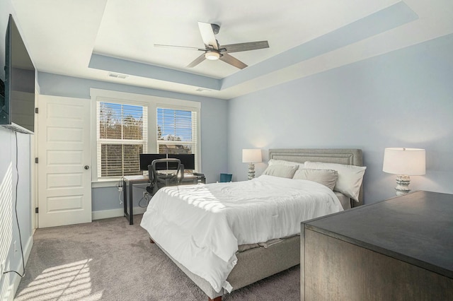 carpeted bedroom with a tray ceiling and ceiling fan