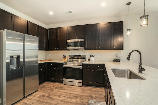 kitchen with sink, light stone counters, light wood-type flooring, appliances with stainless steel finishes, and decorative backsplash