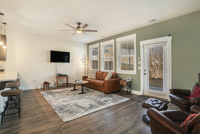 living room with dark wood-type flooring, ceiling fan, and a healthy amount of sunlight