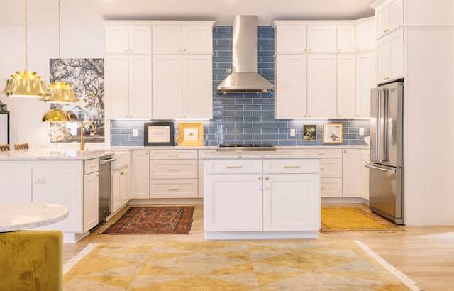 kitchen with white cabinets, wall chimney exhaust hood, light wood-type flooring, appliances with stainless steel finishes, and decorative light fixtures