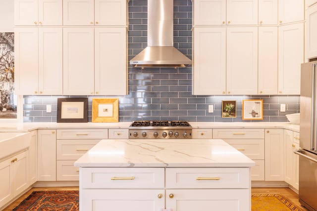 kitchen with light stone countertops, stainless steel appliances, wall chimney range hood, backsplash, and wood-type flooring