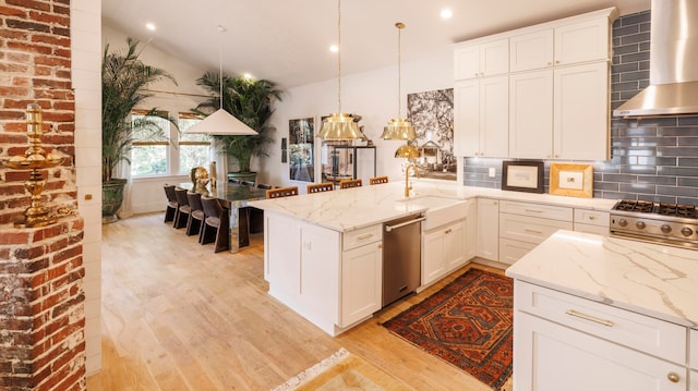 kitchen with light stone countertops, wall chimney exhaust hood, hanging light fixtures, light hardwood / wood-style flooring, and appliances with stainless steel finishes