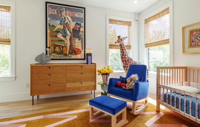 bedroom with multiple windows, light hardwood / wood-style flooring, and a crib