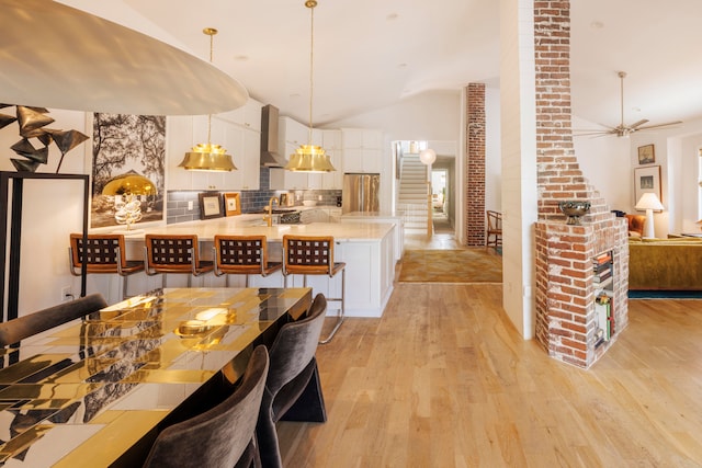 kitchen with backsplash, white cabinets, hanging light fixtures, ceiling fan, and light wood-type flooring