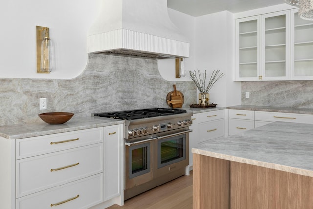 kitchen with range with two ovens, premium range hood, white cabinetry, and glass insert cabinets