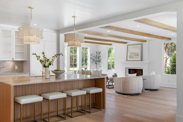 kitchen featuring a chandelier, light wood-style floors, healthy amount of natural light, beamed ceiling, and light stone countertops