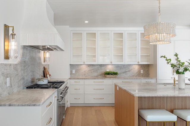 kitchen with stainless steel stove, custom range hood, light stone countertops, light wood-type flooring, and glass insert cabinets