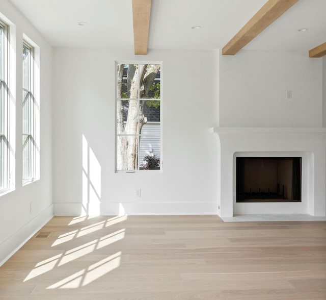 unfurnished living room with beamed ceiling, wood finished floors, a fireplace with flush hearth, and baseboards