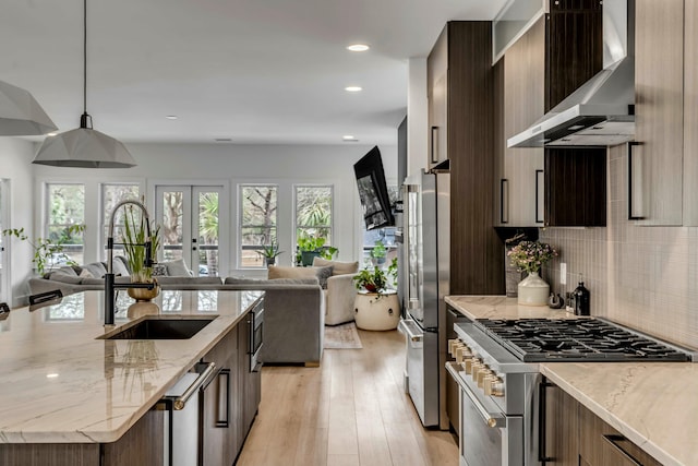 kitchen featuring pendant lighting, wall chimney range hood, stainless steel appliances, light stone counters, and light hardwood / wood-style floors