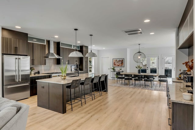 kitchen featuring appliances with stainless steel finishes, decorative light fixtures, dark brown cabinets, and wall chimney range hood