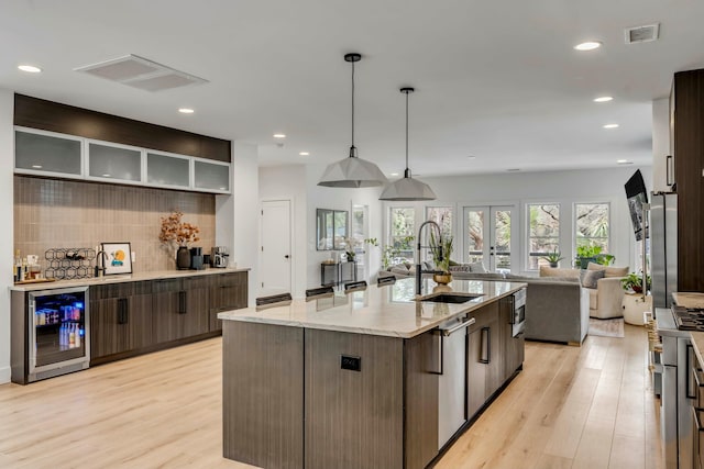 kitchen featuring wine cooler, light stone counters, light wood-type flooring, a large island with sink, and pendant lighting