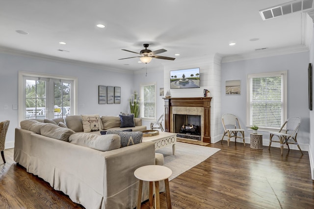 living room featuring ceiling fan, crown molding, a fireplace, and dark wood-type flooring