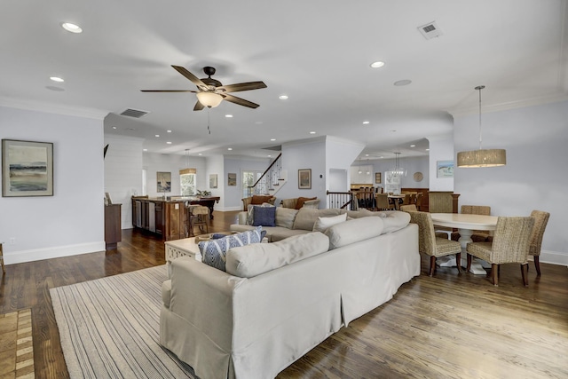 living room featuring ceiling fan with notable chandelier, ornamental molding, and dark wood-type flooring