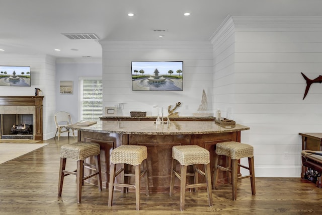 bar with a tile fireplace, dark hardwood / wood-style floors, light stone counters, and ornamental molding