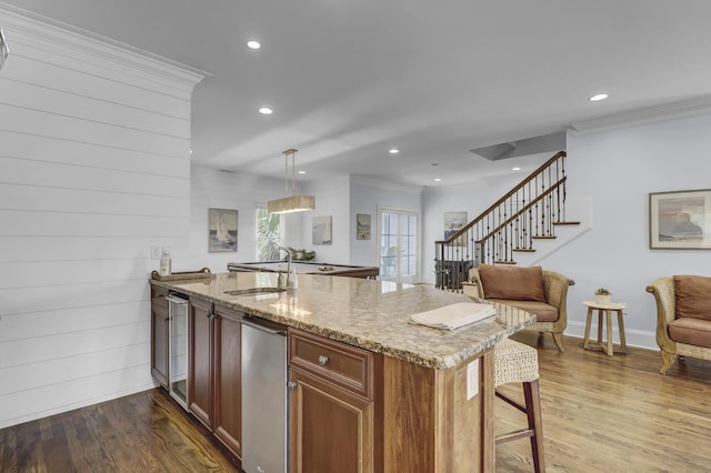 kitchen with light stone countertops, kitchen peninsula, ornamental molding, hardwood / wood-style floors, and hanging light fixtures