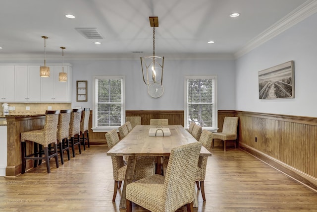 dining room with light hardwood / wood-style flooring, ornamental molding, and wood walls