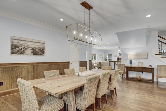 dining space with wood-type flooring, ceiling fan with notable chandelier, ornamental molding, and wood walls