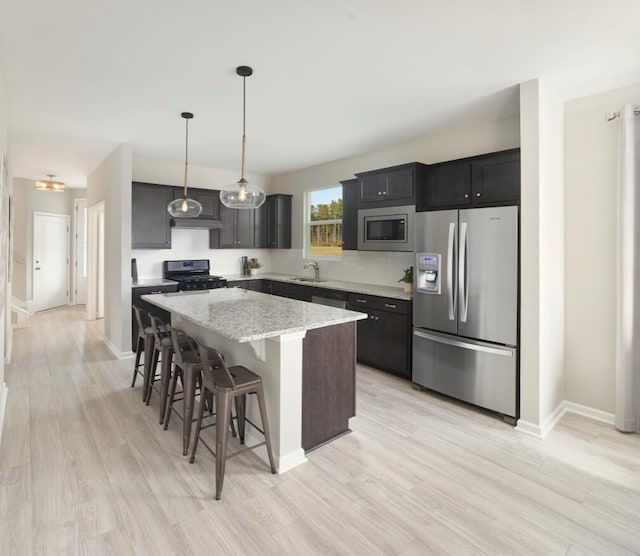 kitchen with appliances with stainless steel finishes, hanging light fixtures, a kitchen bar, a kitchen island, and sink