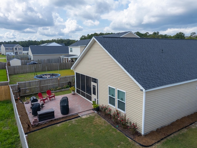 rear view of property featuring a sunroom, a yard, a patio, and an outdoor fire pit