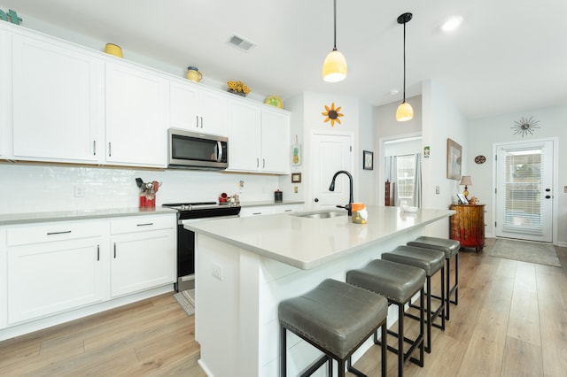 kitchen with an island with sink, light wood-type flooring, white cabinetry, and appliances with stainless steel finishes