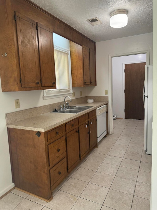 kitchen featuring a textured ceiling, white appliances, light tile patterned floors, and sink