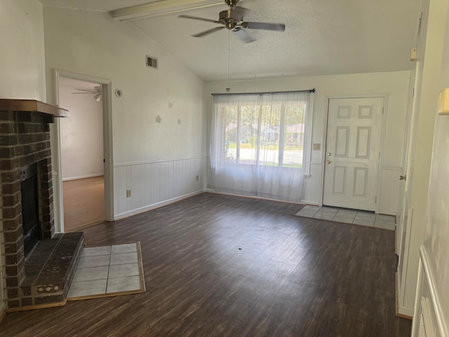 unfurnished living room with dark hardwood / wood-style flooring, a textured ceiling, ceiling fan, lofted ceiling with beams, and a fireplace