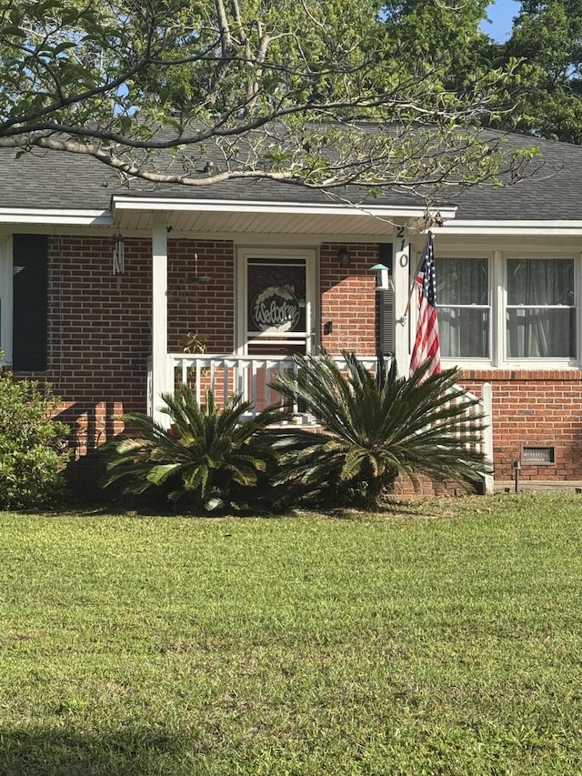 doorway to property with roof with shingles, a yard, and brick siding