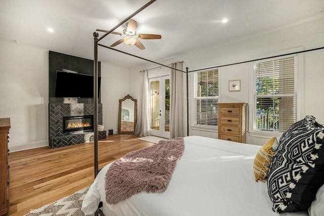 bedroom featuring access to outside, light wood-type flooring, ornamental molding, ceiling fan, and a tiled fireplace